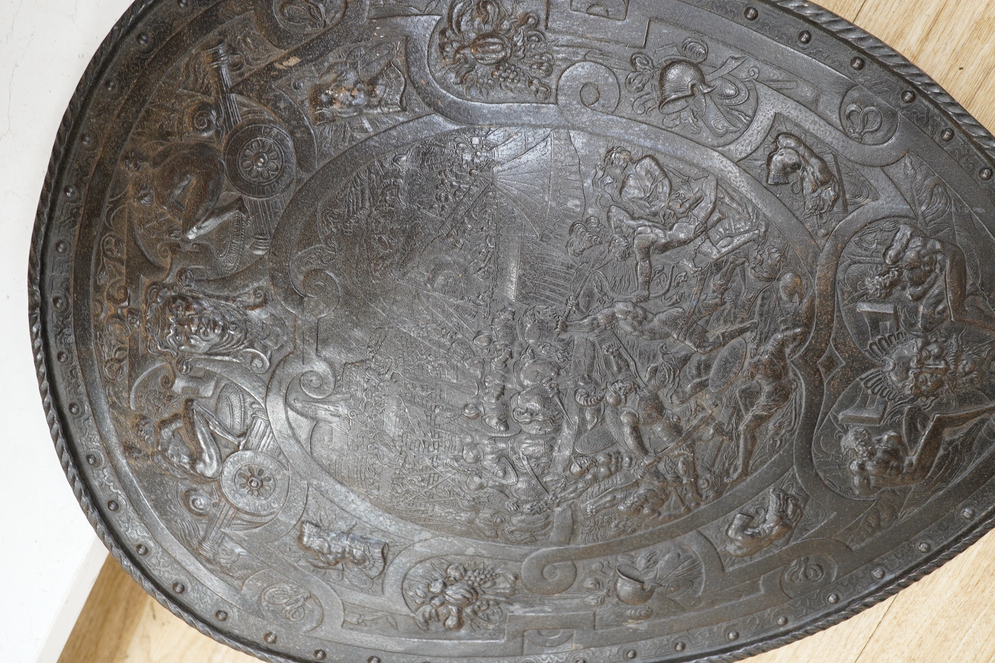 A decorative late 19th century cast iron shield in a romantic style, scene incorporates classical battles surrounded by masks captives, cannon and fruit, 60 x 42.5cm. Condition - good